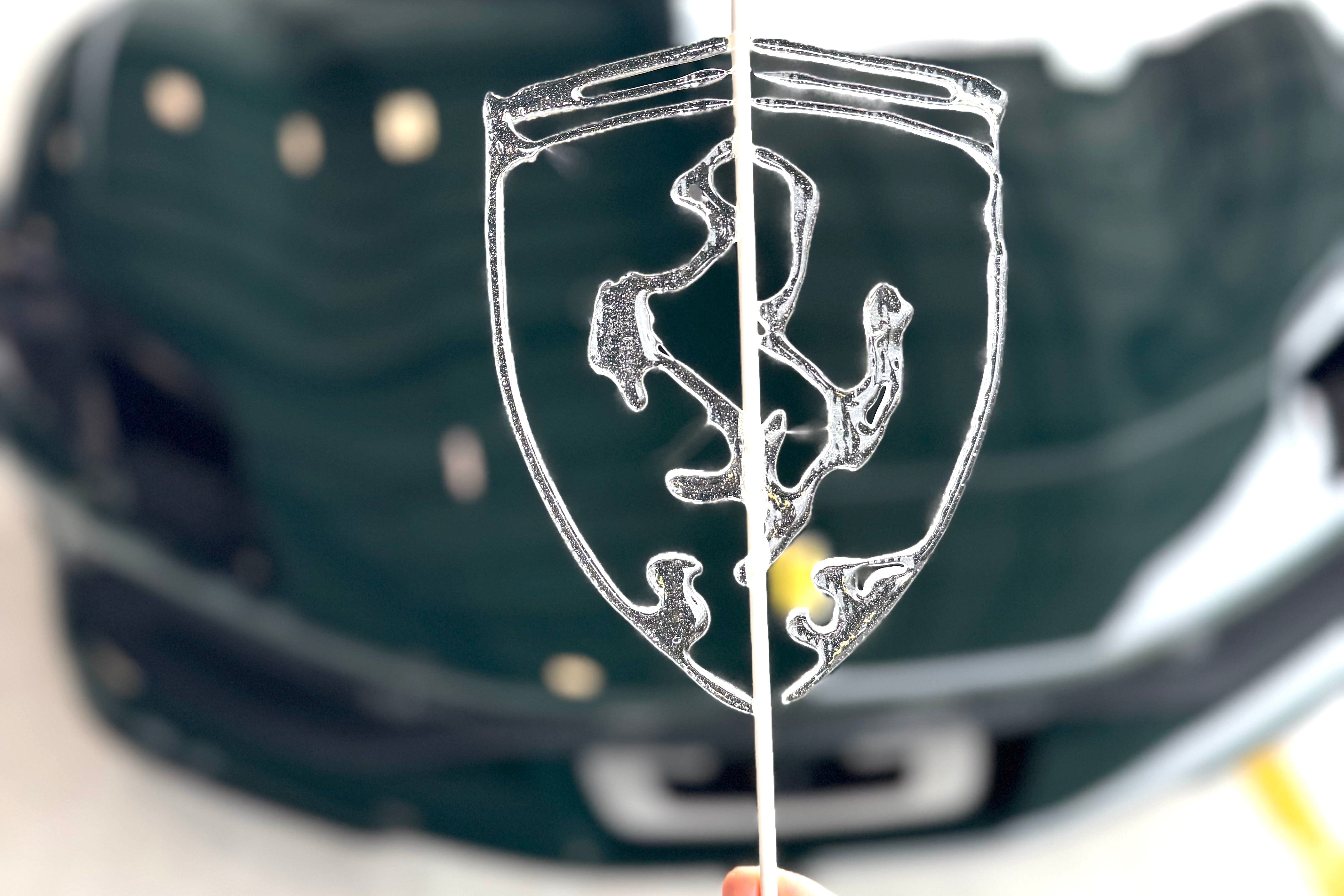 Hand holding a clear Ferrari logo lollipop in front of a blurred Ferrari car